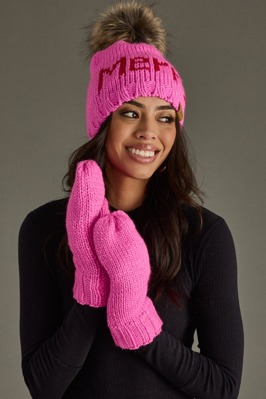 Woman wearing a pink knit hat and mittens with a gray background