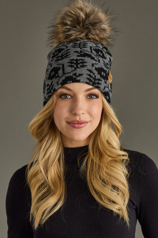 Woman wearing a patterned beanie with a pom-pom against a neutral background