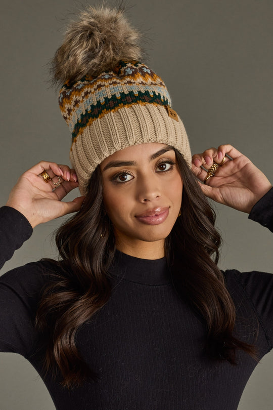 Woman wearing a patterned beanie with a pom-pom against a neutral background