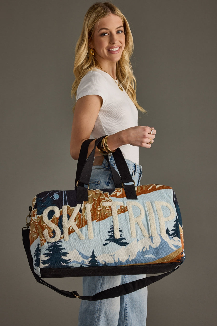 Woman holding a large duffel bag with 'Ski Trip' text against a gray background