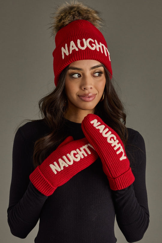 Person wearing a red 'NAUGHTY' beanie and mittens against a gray background