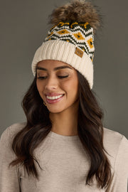 Woman wearing a patterned beanie with a fur pom-pom on a gray background