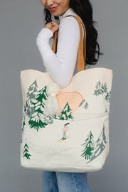 Person holding a tote bag with a forest design and a skiing person.
