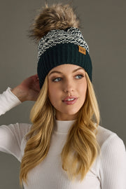 Woman wearing a dark teal and white patterned beanie with a pom-pom on a gray background