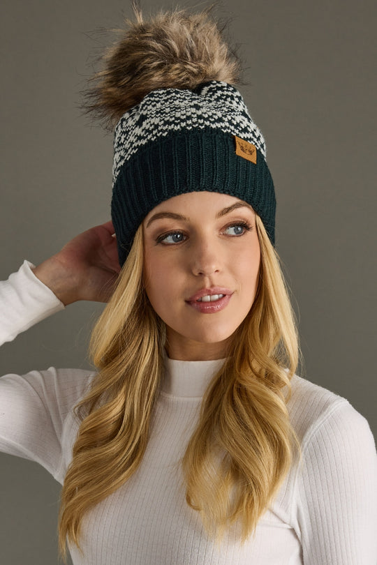 Woman wearing a dark teal and white patterned beanie with a pom-pom on a gray background