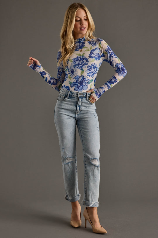 Woman wearing a floral top and jeans on a gray background
