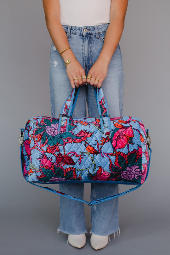 Person holding a floral duffel bag against a gray background