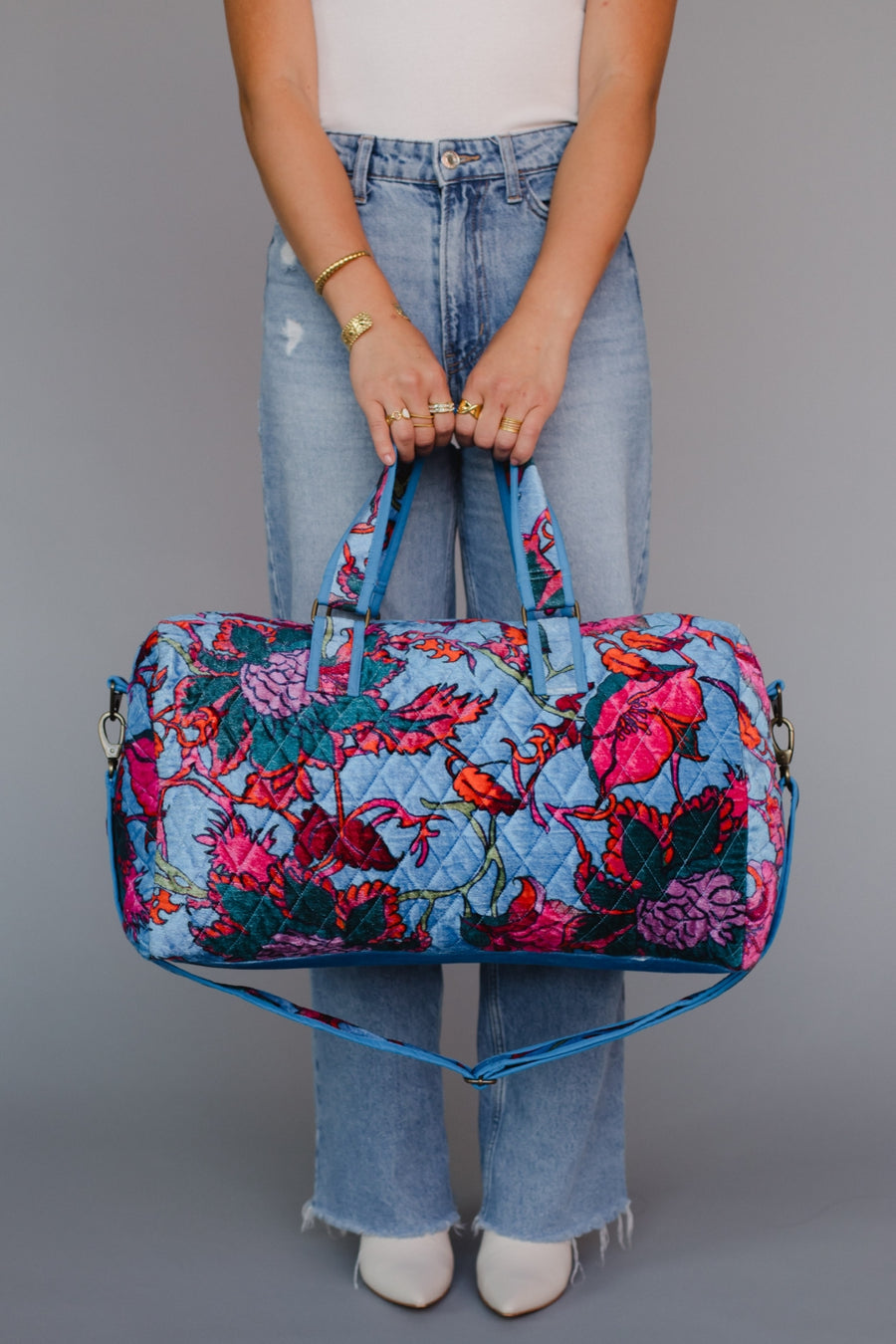 Person holding a floral duffel bag against a gray background