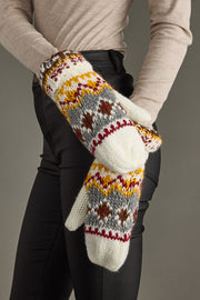 Pair of knit mittens with a pattern held by a person against a neutral background