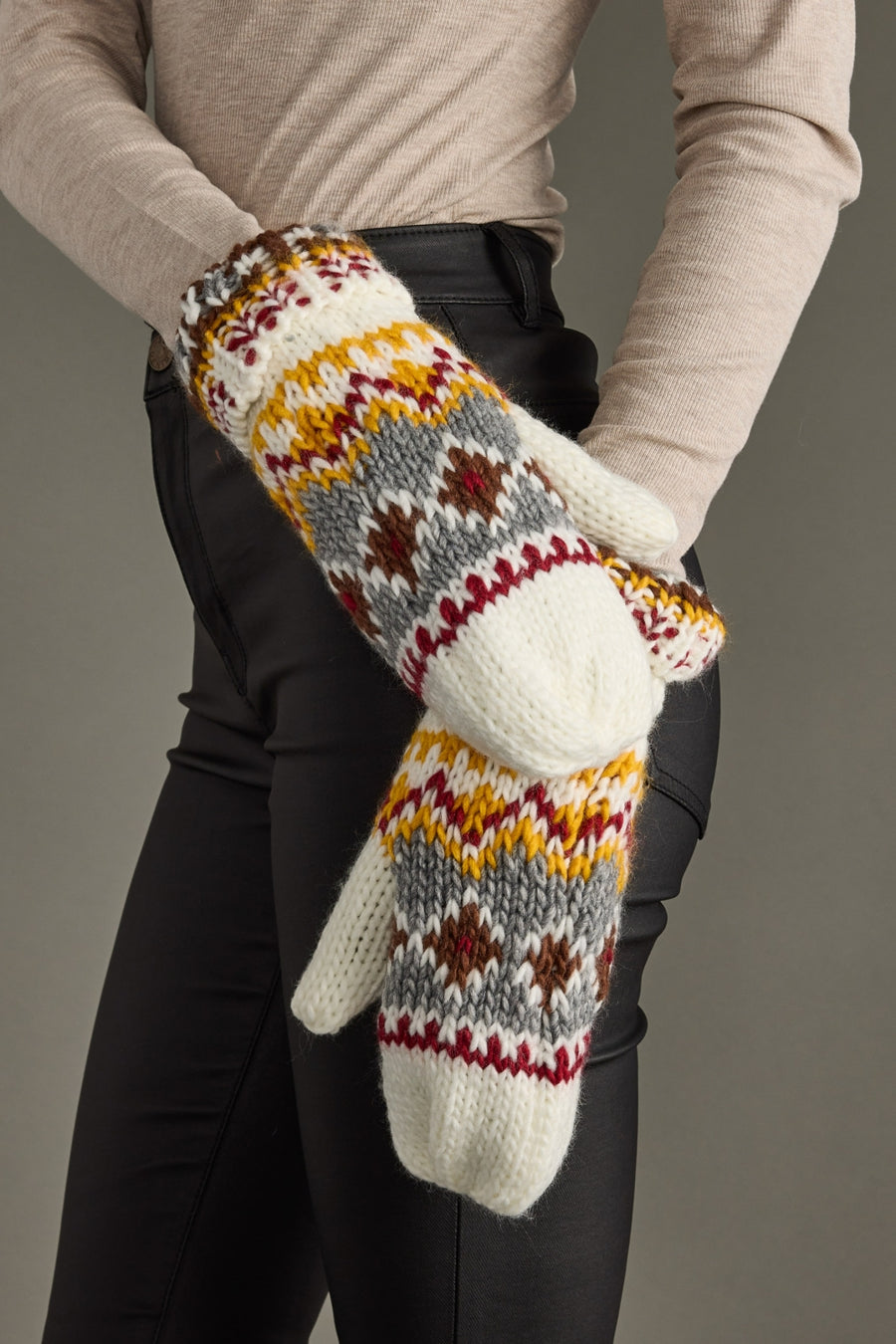 Pair of knit mittens with a pattern held by a person against a neutral background