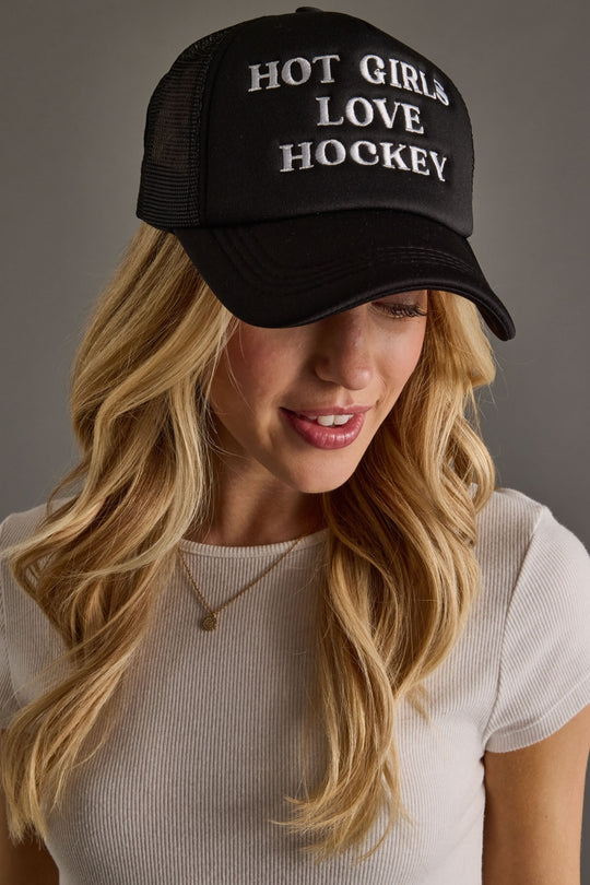 Woman wearing a black cap with 'Hot Girls Love Hockey' text against a gray background
