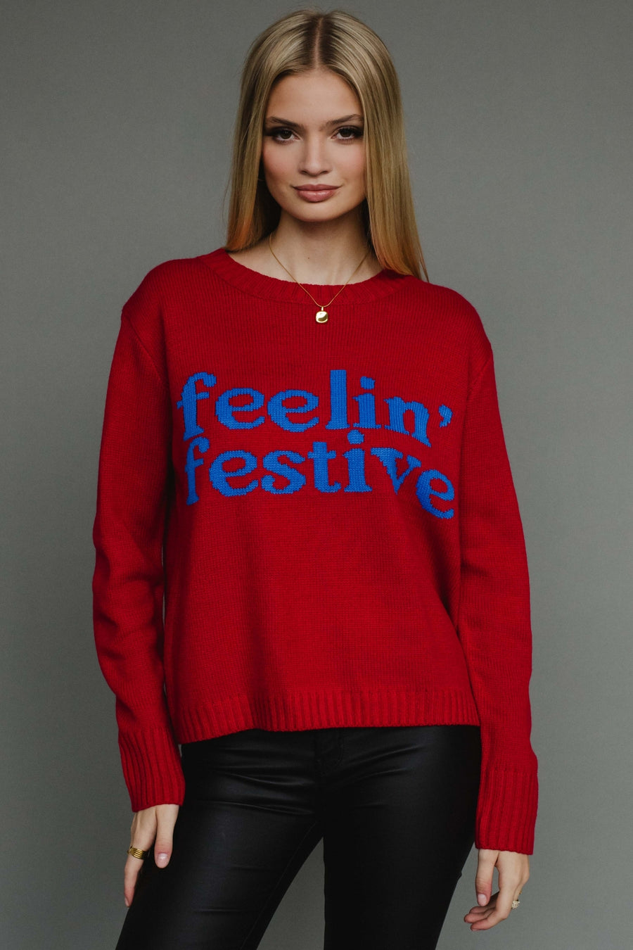 Woman wearing a red sweater with 'feelin' festive' text on a gray background