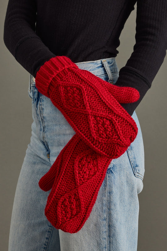 Red knitted gloves worn by a person against a neutral background