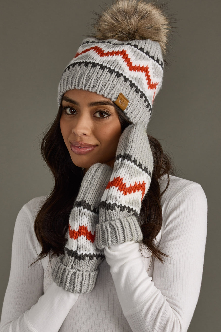 Woman wearing a gray knit hat and mittens with a pom-pom on a gray background
