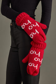 Red knitted gloves with white text worn by a person against a gray background