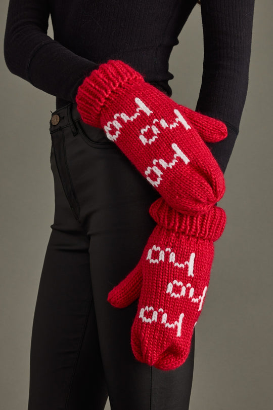 Red knitted gloves with white text worn by a person against a gray background