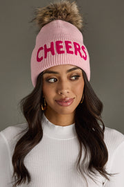 Woman wearing a pink beanie with 'CHEERS' in pink letters on a gray background
