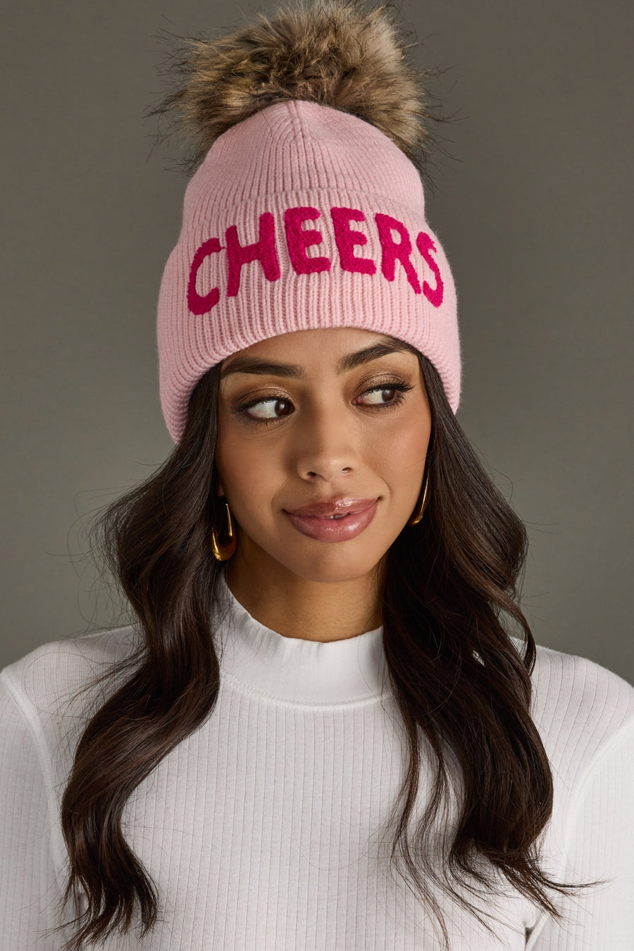 Woman wearing a pink beanie with 'CHEERS' in pink letters on a gray background