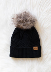 Black knit beanie with fur pom-pom on a white textured background