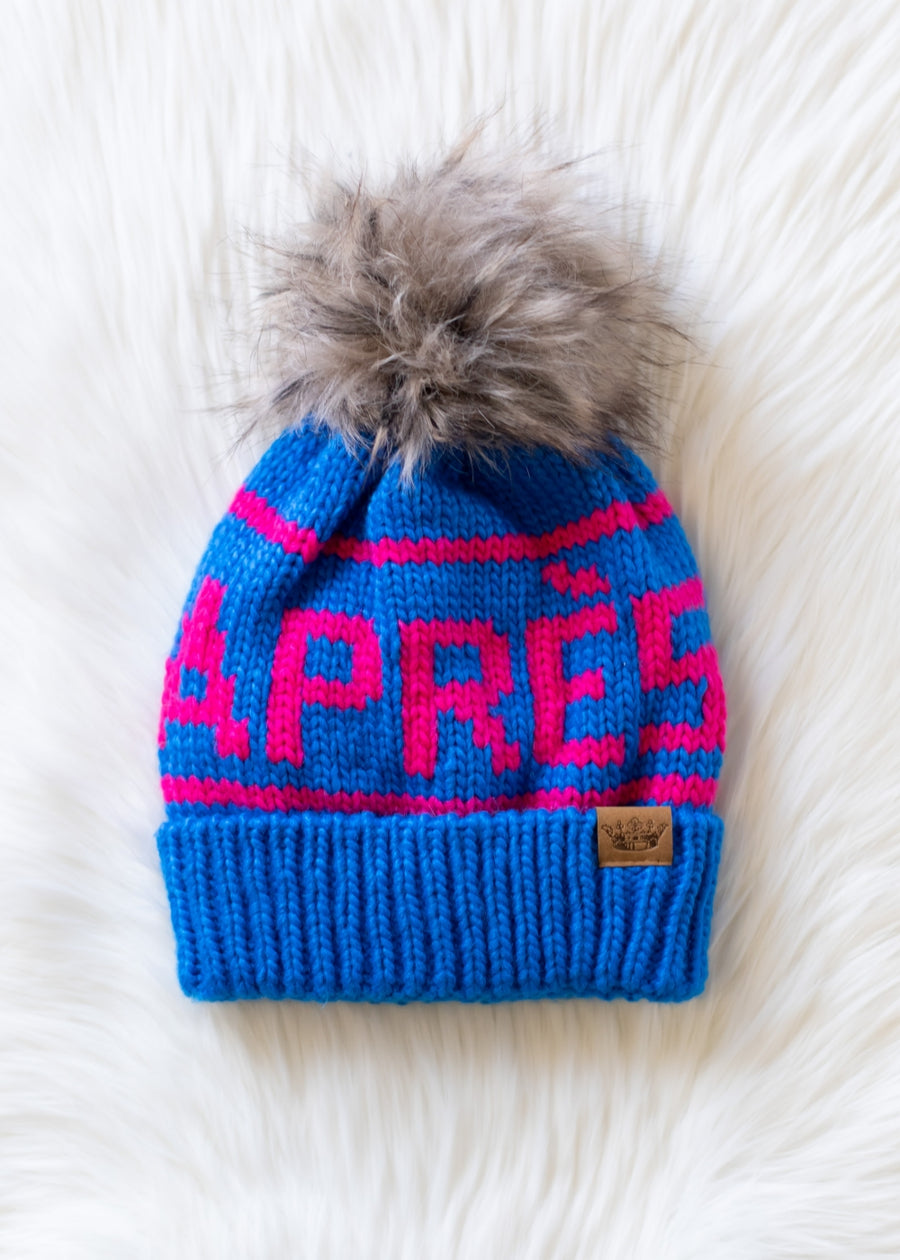 Blue knit beanie with pink text and gray pom-pom on a white background