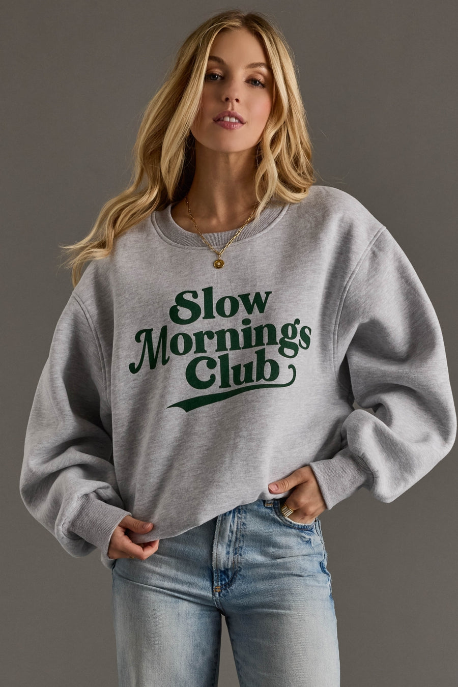 Woman wearing a gray sweatshirt with 'Slow mornings club' text on a plain background