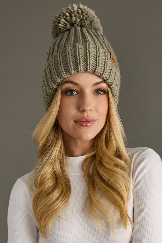 Woman wearing a knitted beanie with a pom-pom against a neutral background