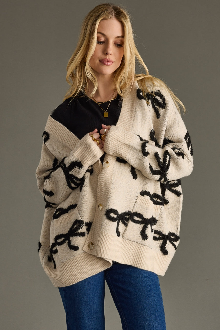 Woman wearing a beige cardigan with black bow patterns on a gray background