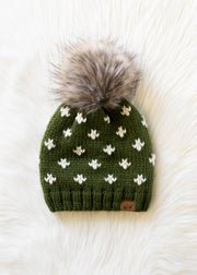 Green knit beanie with white patterns and a gray pom-pom on a white fur background