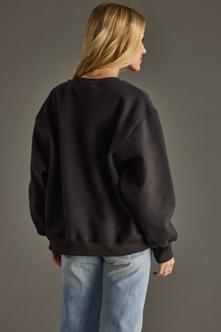 Person wearing a black sweatshirt and blue jeans against a gray background