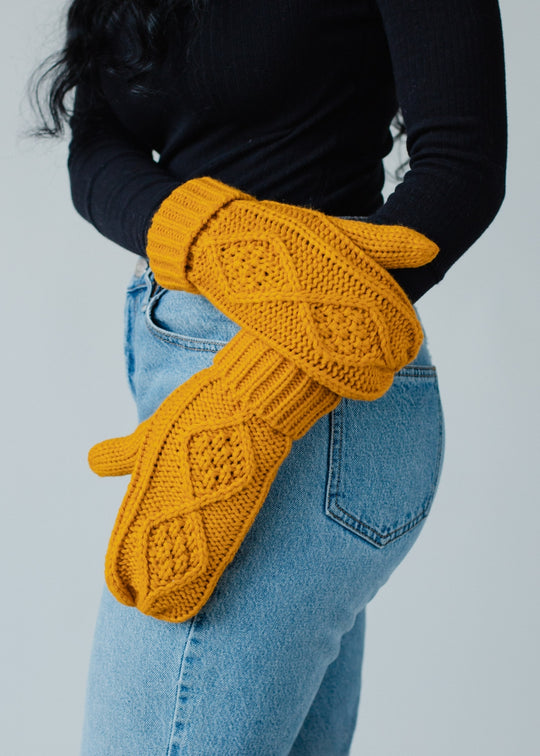 Person wearing mustard yellow knitted gloves with a plain background