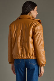 Woman wearing a brown leather jacket and blue jeans against a gray background