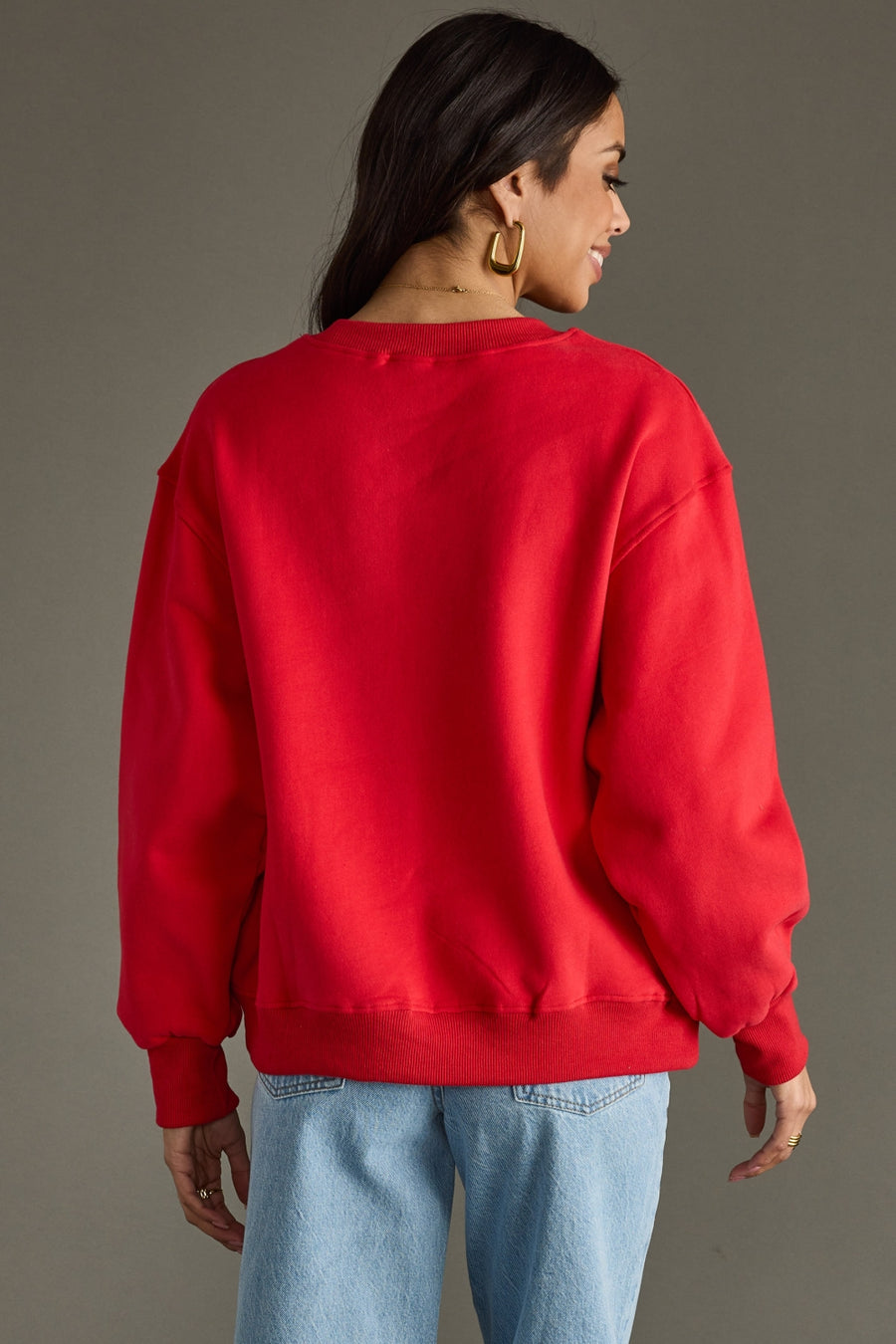 Person wearing a red sweatshirt and blue jeans against a gray background