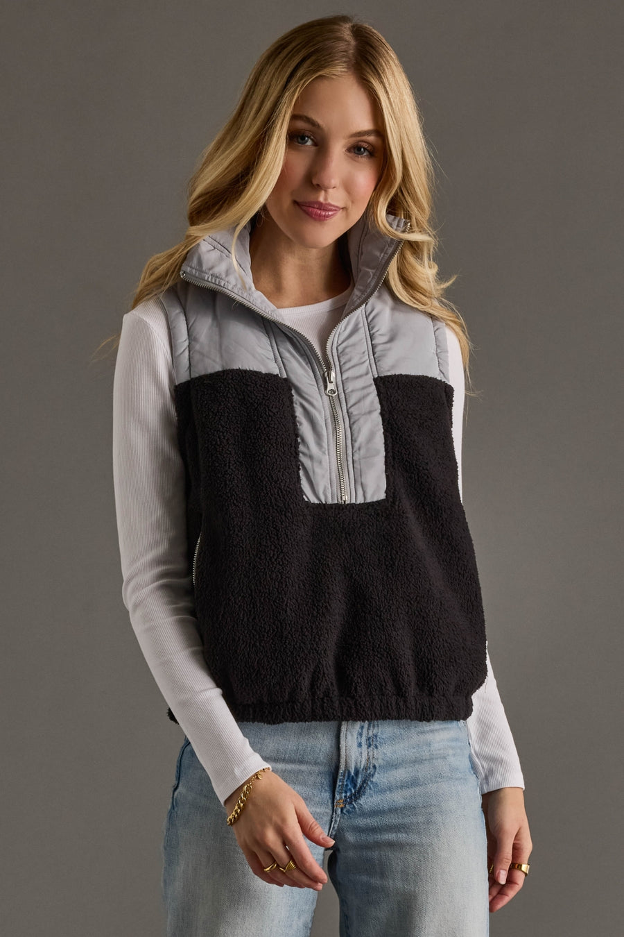 Woman wearing a black and gray half-zip sweater vest on a gray background