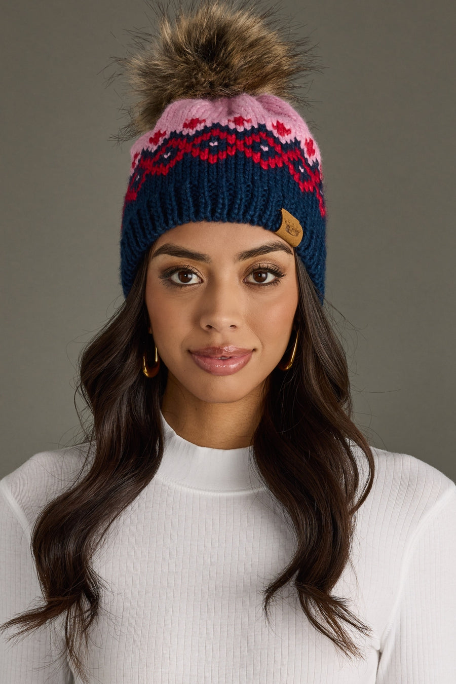 Woman wearing a colorful knit beanie with a pom-pom against a gray background