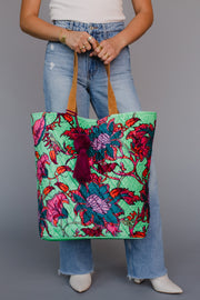 Person holding a colorful floral tote bag against a gray background