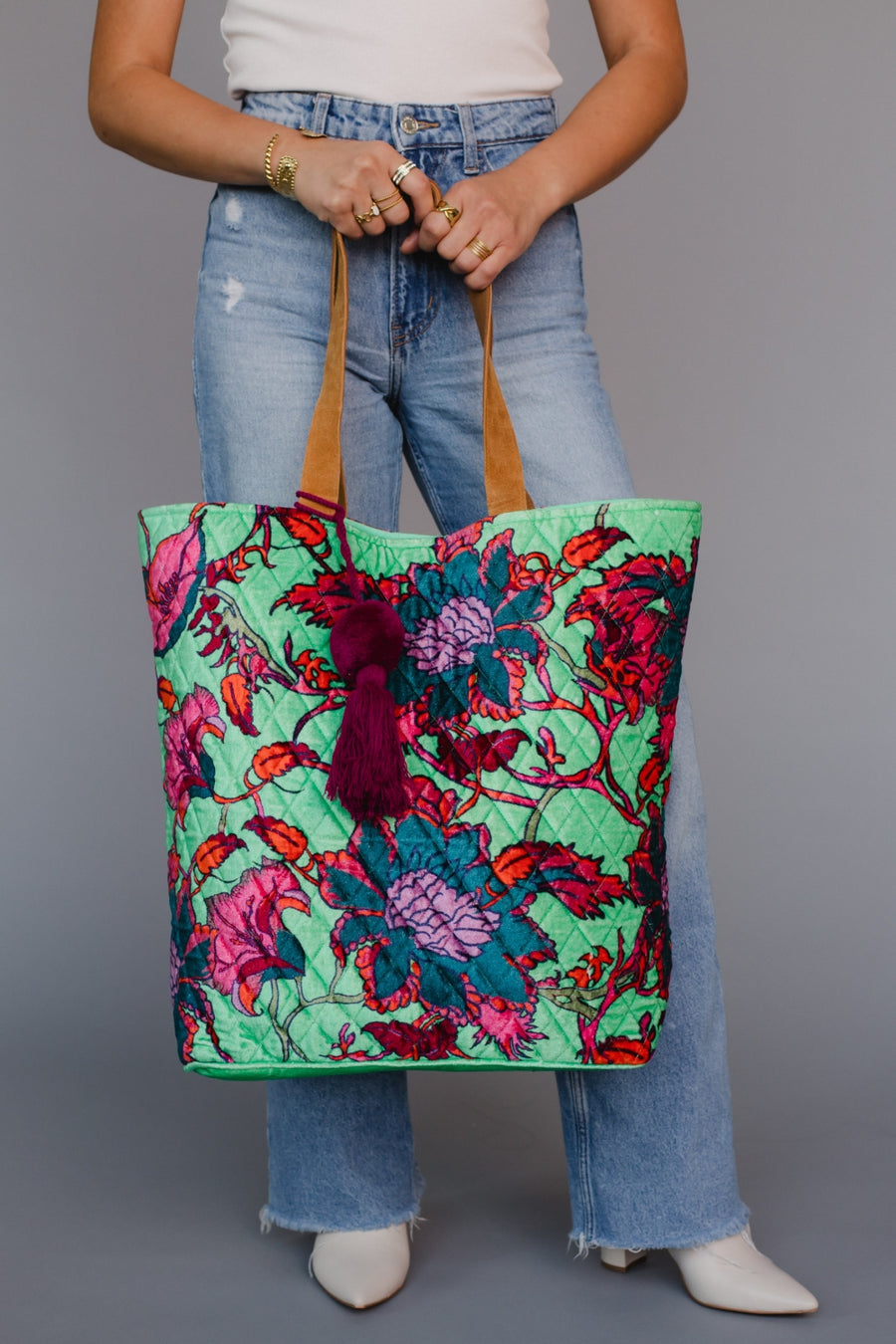 Person holding a colorful floral tote bag against a gray background