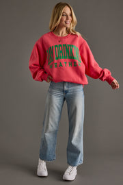 Person wearing a coral sweatshirt with text and blue jeans on a gray background