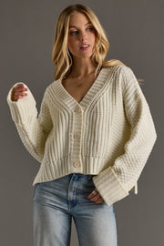 Woman wearing a cream knitted cardigan and jeans against a gray background