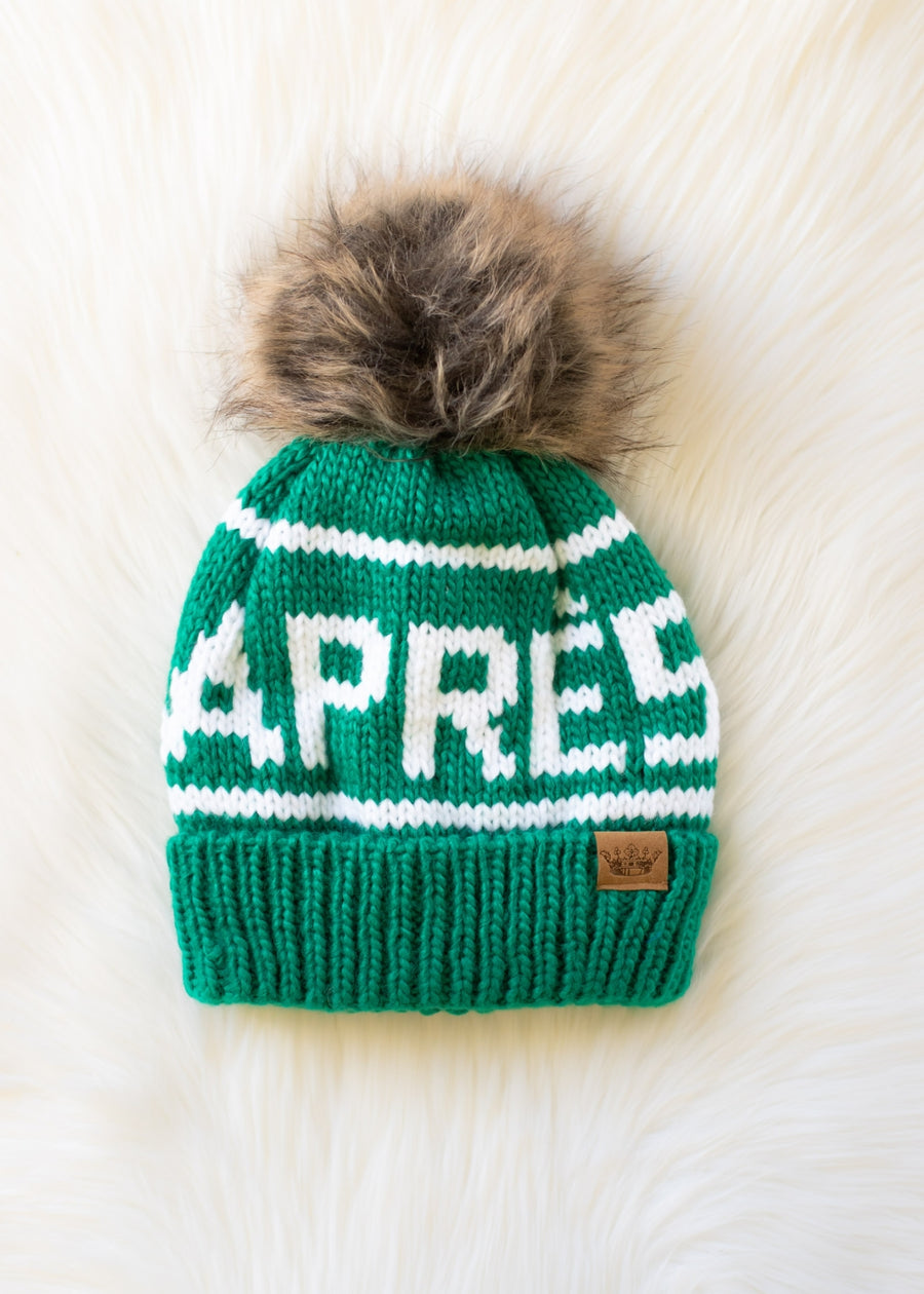 Green knit pet beanie with white text and fur pom-pom on a white background