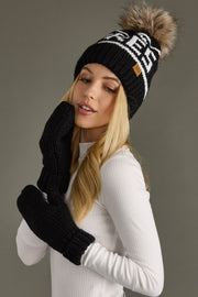 Woman wearing a black knit beanie with a pom-pom and black gloves against a gray background