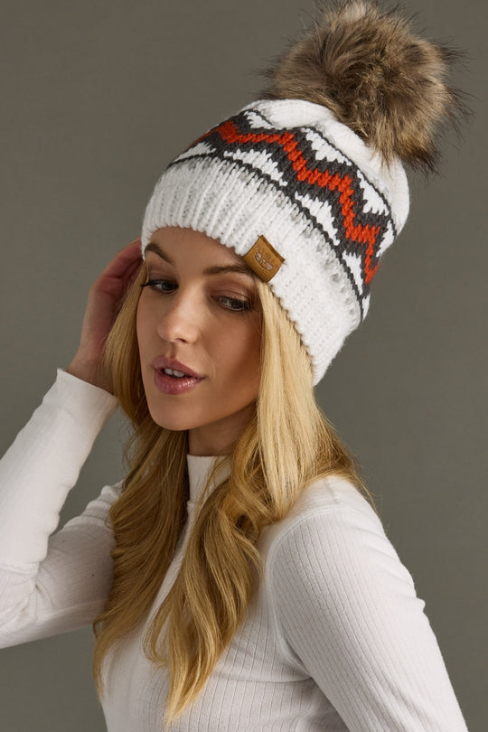 Woman wearing a white knit beanie with a fur pom-pom on a gray background