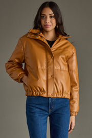 Woman wearing a brown leather jacket and blue jeans against a gray background