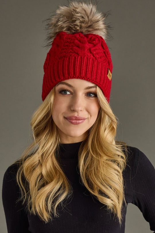 Woman wearing a red knit beanie with a fur pom-pom against a gray background