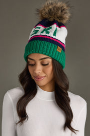Woman wearing a colorful knit beanie with a fur pom-pom on a gray background