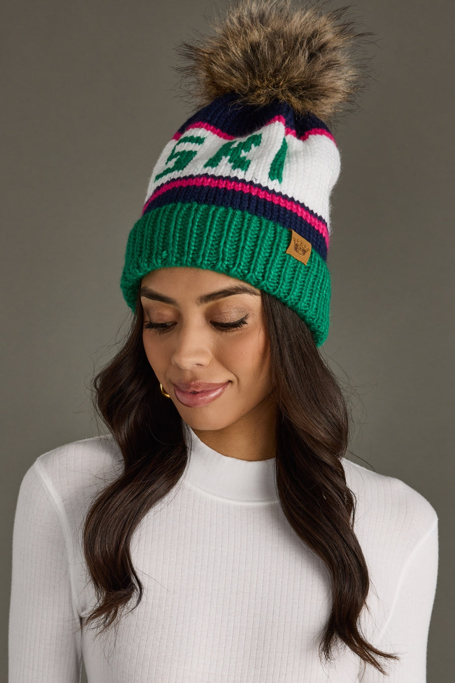 Woman wearing a colorful knit beanie with a fur pom-pom on a gray background