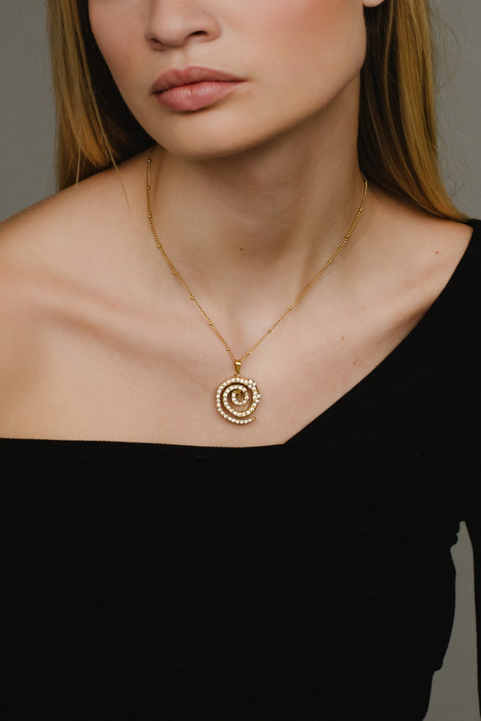 Close-up of a woman wearing a gold necklace with a spiral pendant against a neutral background
