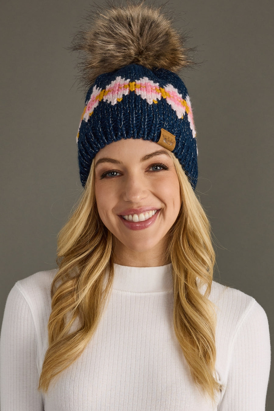 Woman wearing a blue knit beanie with a pom-pom against a gray background