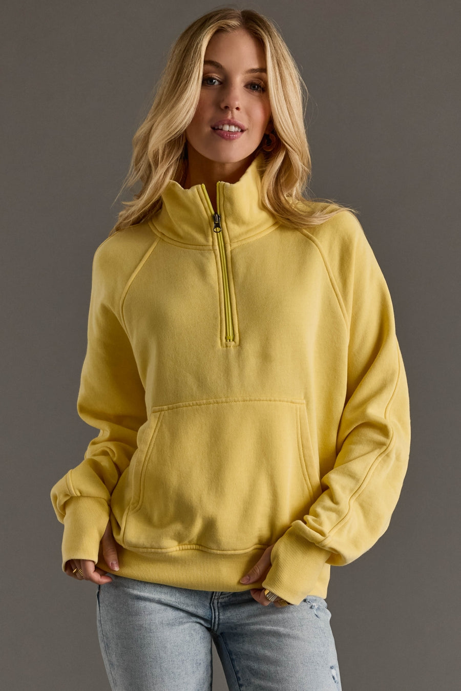 Woman wearing a yellow pullover with a zipper on a gray background