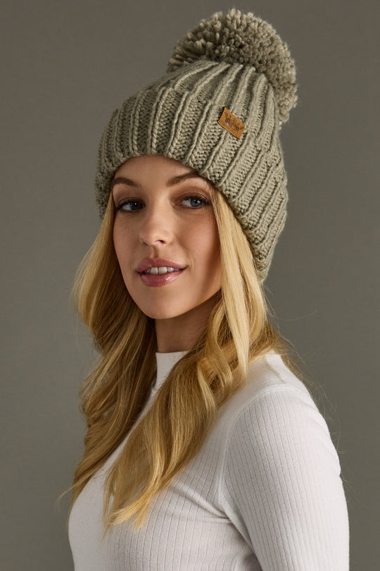 Woman wearing a knitted beanie with a pom-pom against a gray background