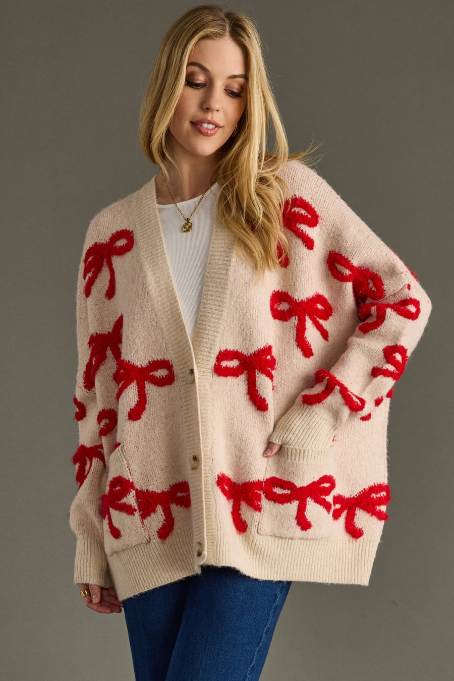 Woman wearing a beige cardigan with red bow patterns on a gray background